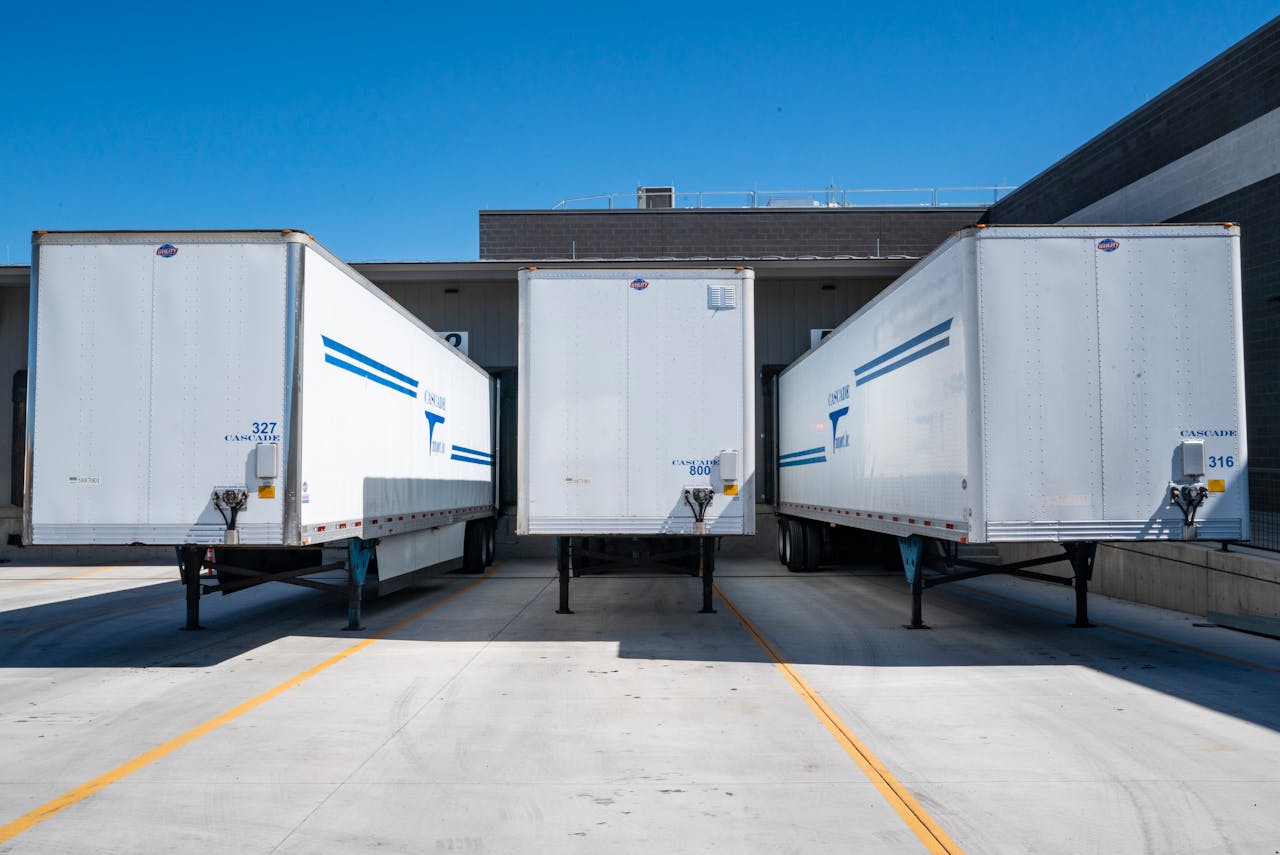 fitness-service-01 Three white cargo trailers parked at an industrial shipping dock under clear blue skies.